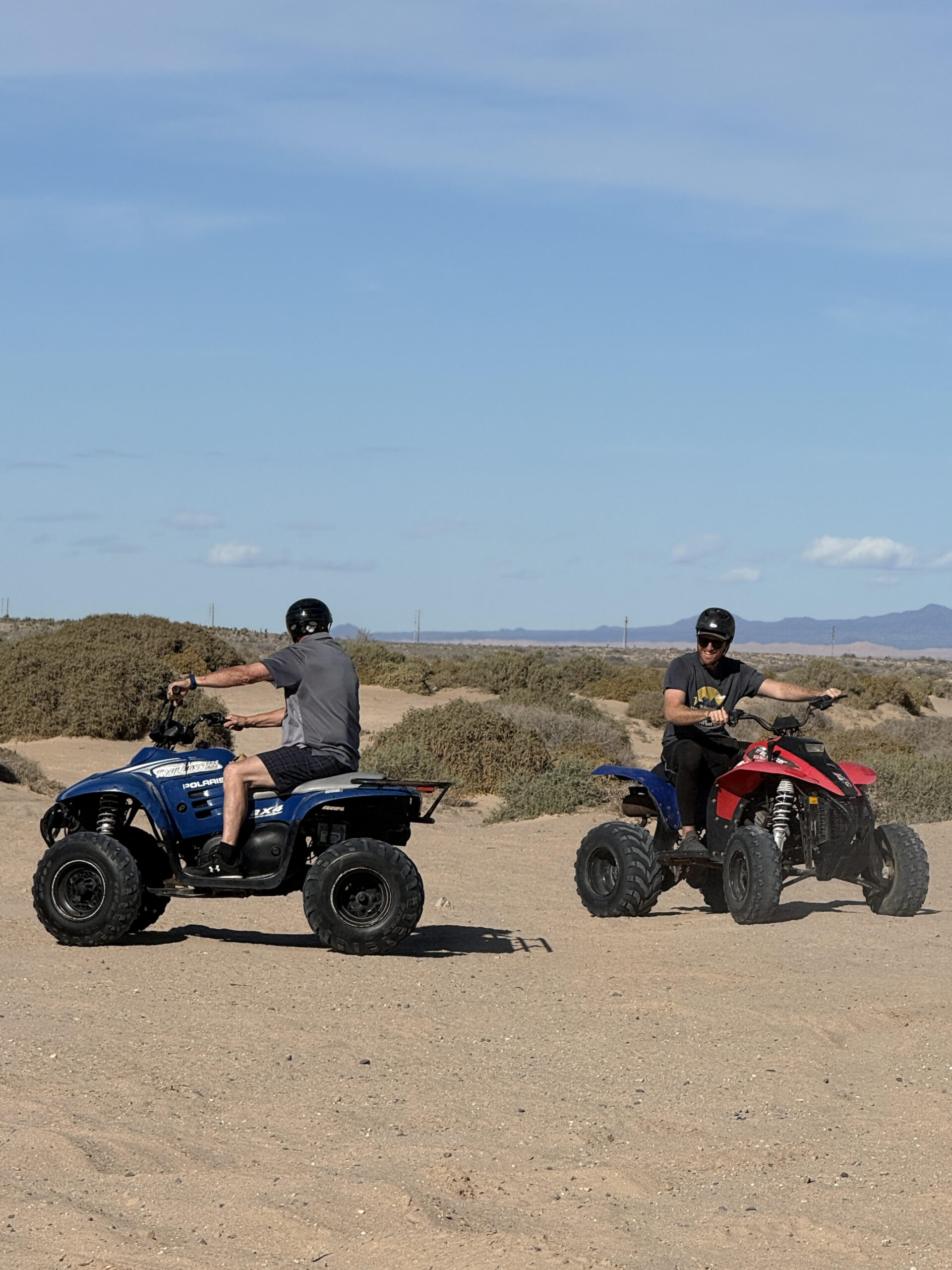 Two men on ATVs together, dust and desert